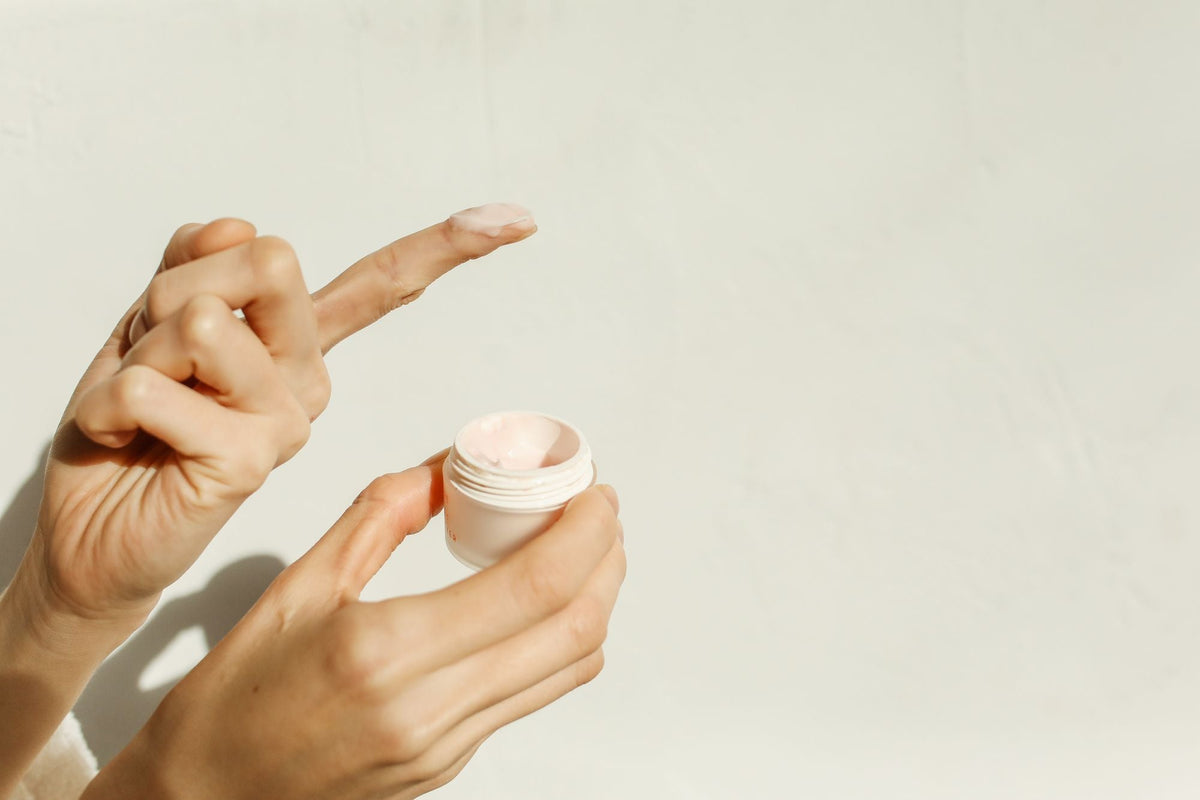 Manos con una pequeña porción de crema hidratante en la yema del dedo, sobre fondo claro