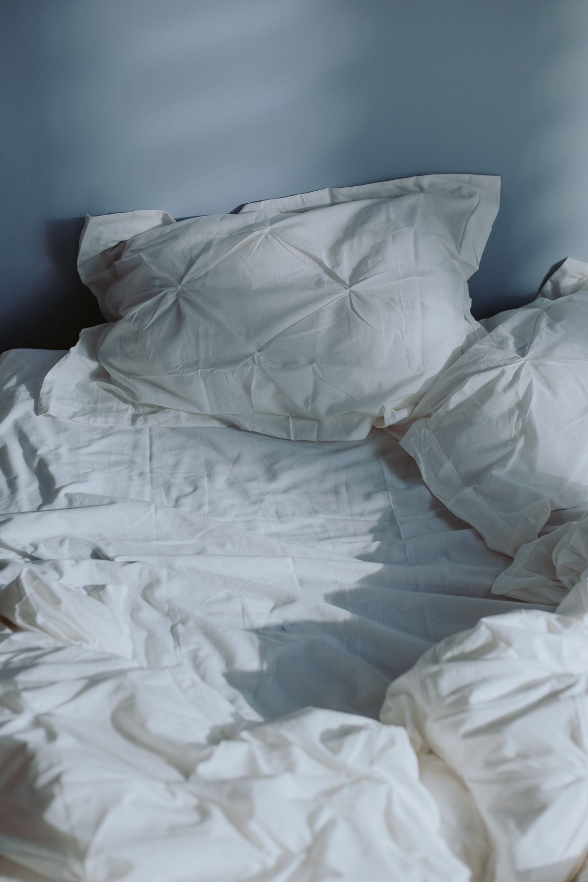 Cama con sábanas blancas arrugadas y almohada bajo la luz de la mañana, sobre la relación entre dormir bien y la piel