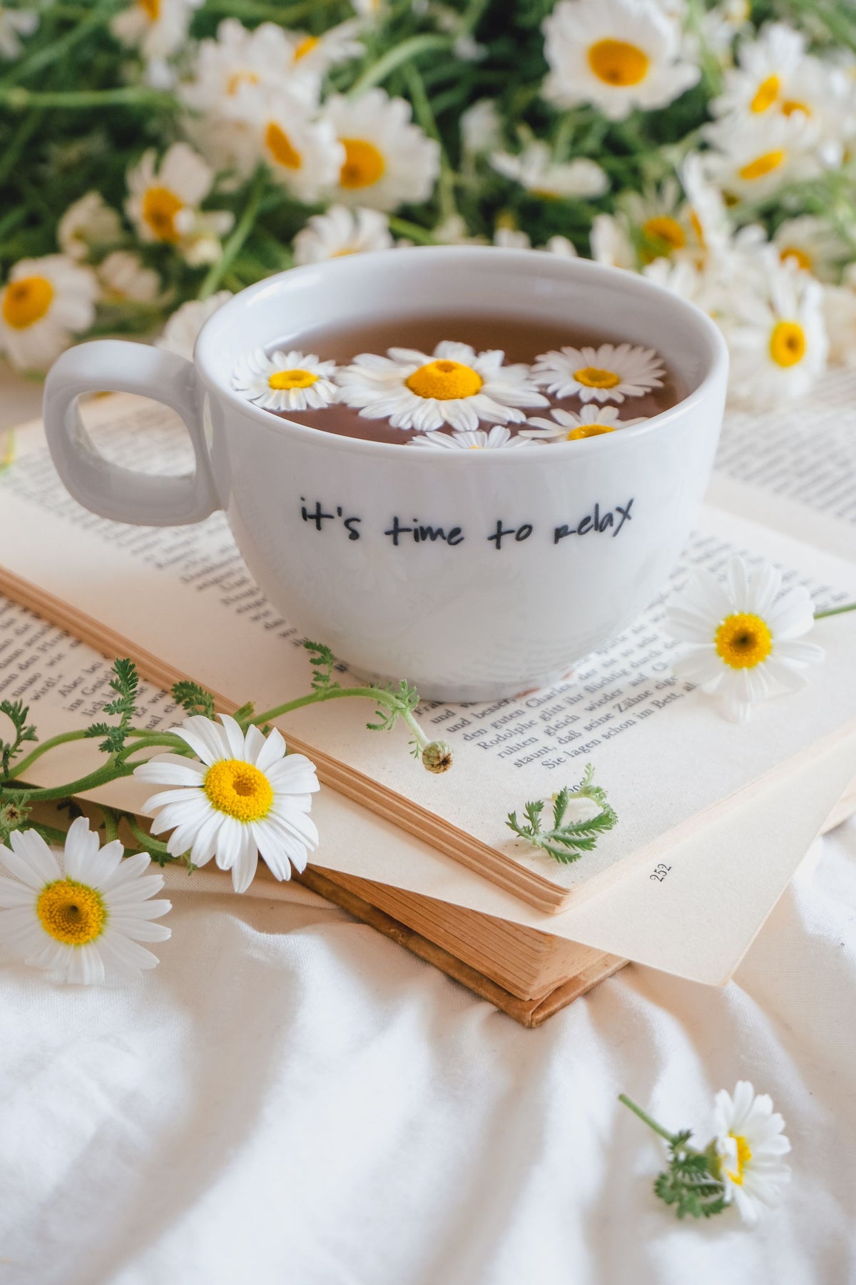 Taza de té de manzanilla con flores de manzanilla y un libro abierto, para un artículo sobre ciclo menstrual y piel