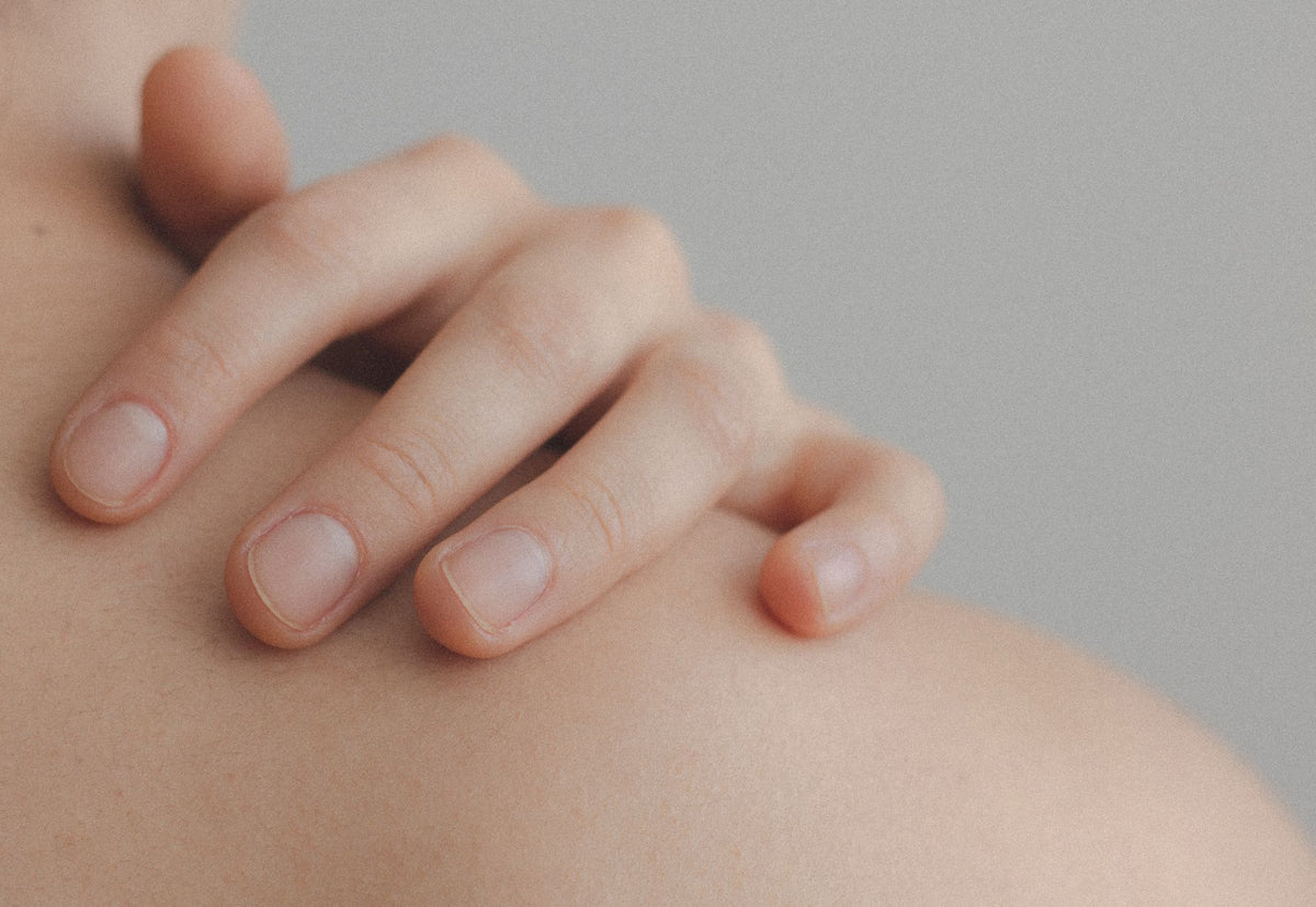 Mano sobre el hombro de una mujer con luz cálida que deja ver la textura de la piel