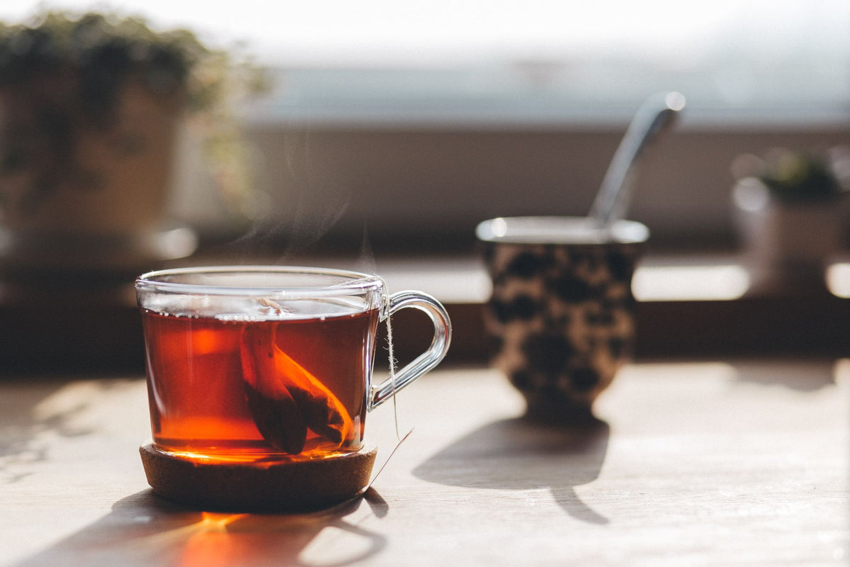 Taza de vidrio con té humeante bajo luz cálida, sobre la relación entre cortisol, estrés y piel