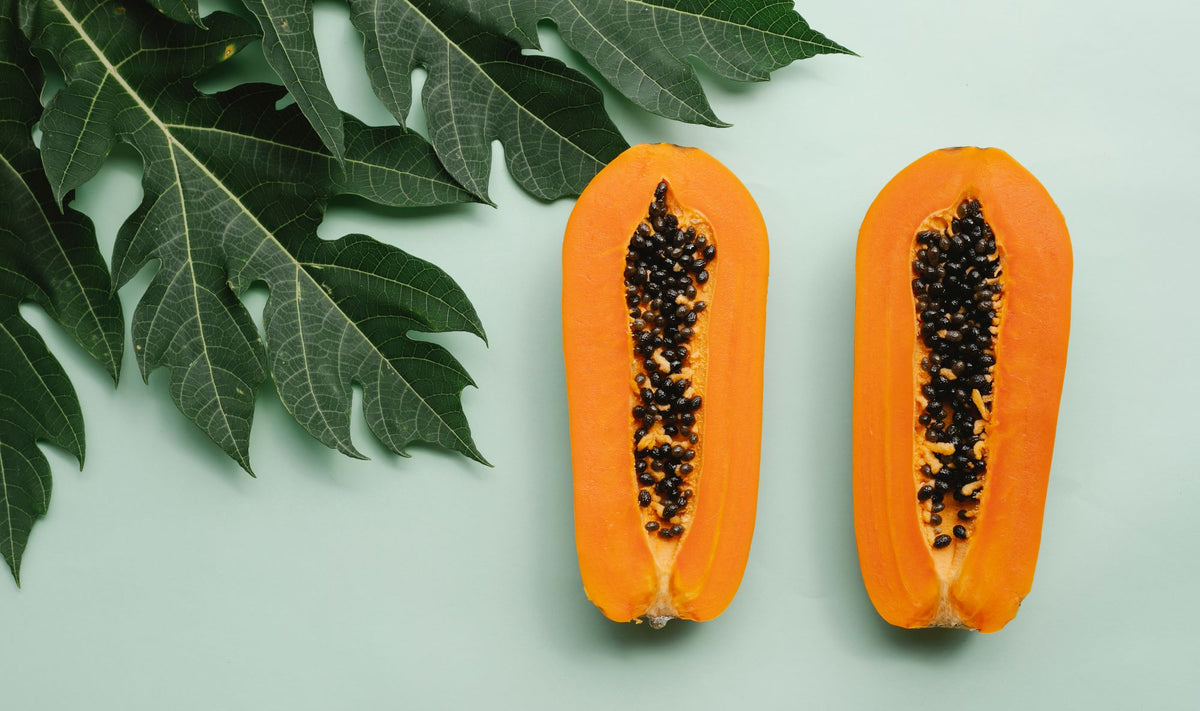 Papaya partida a la mitad con sus semillas negras junto a hojas verdes, para un artículo sobre ácido salicílico