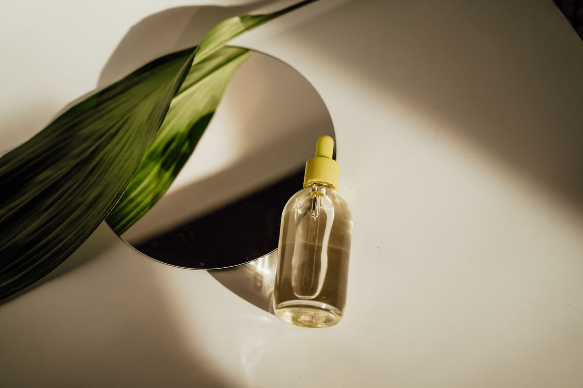 Frasco gotero de vidrio transparente con sérum junto a un espejo redondo, con luz natural