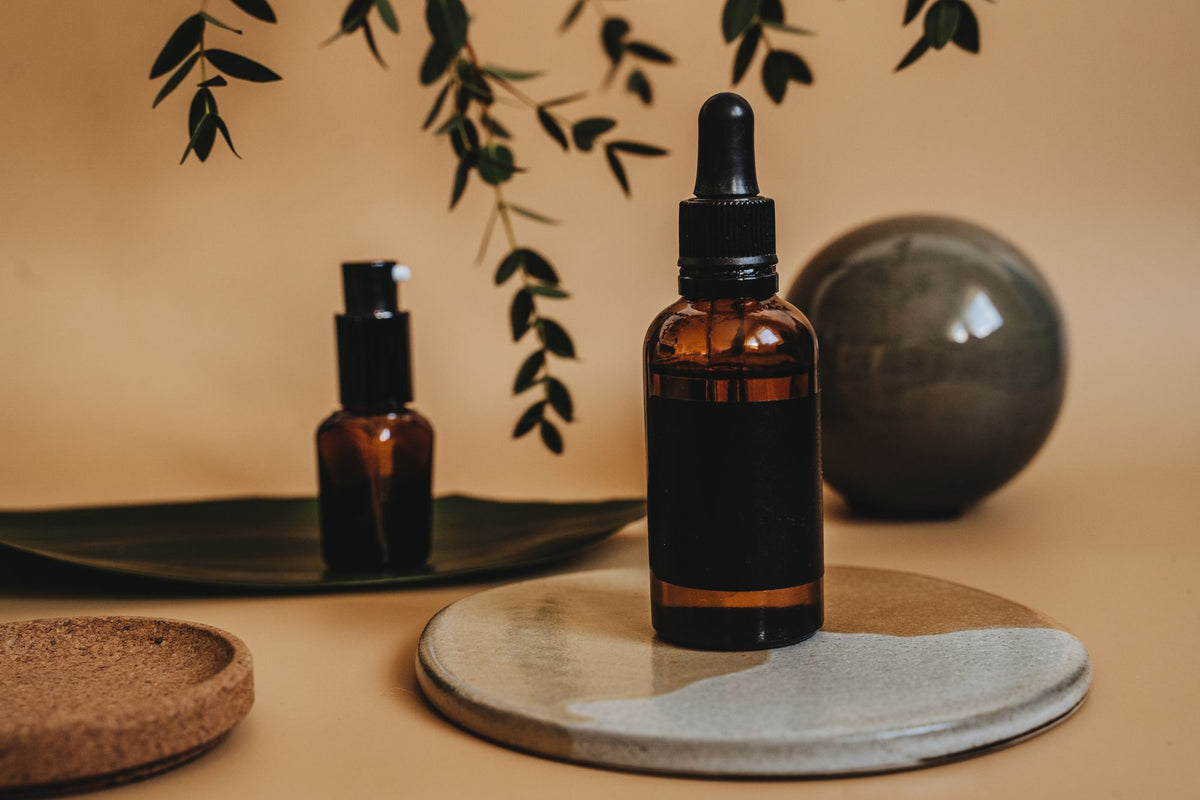 Frascos gotero de vidrio ámbar con hojas verdes y texturas naturales, para un artículo sobre cómo combinar niacinamida, vitamina C y ácidos