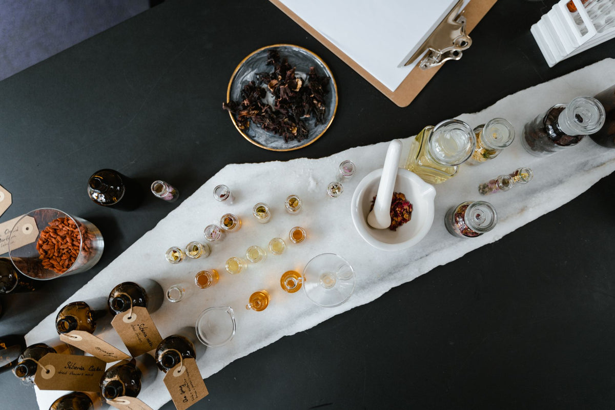 Frascos de vidrio con líquidos dorados e ingredientes botánicos sobre una mesa, vistos desde arriba